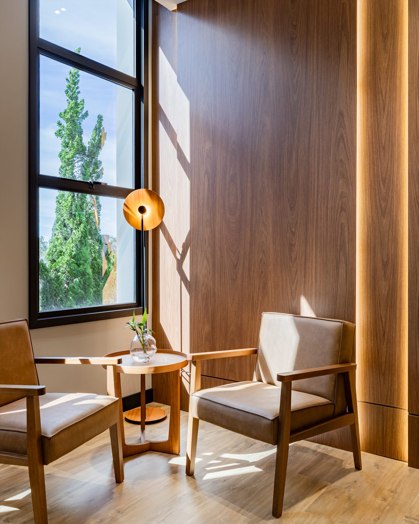 Área de espera junto à janela, com duas poltronas e iluminação natural.